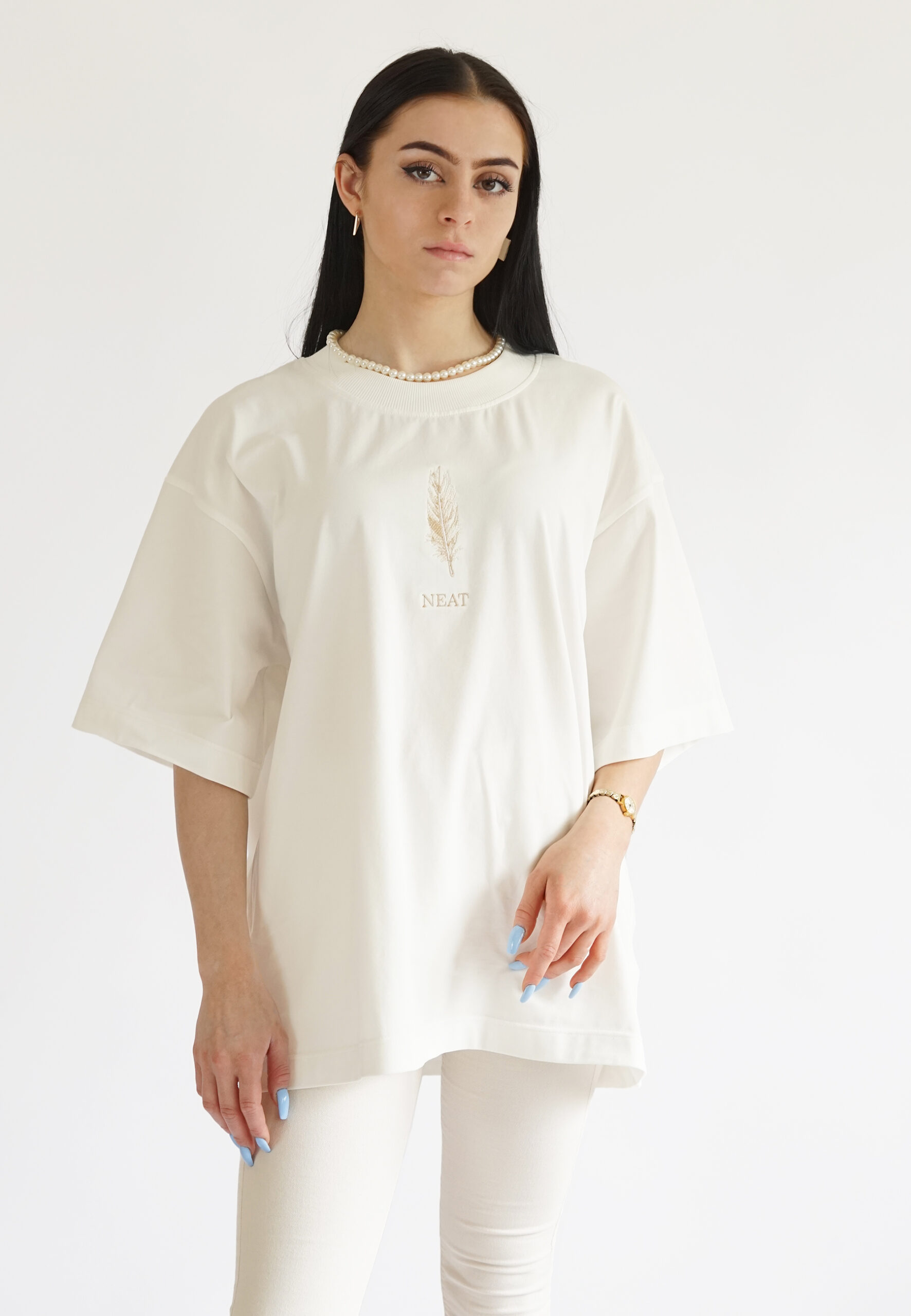 cream-colored oversized t-shirt with subtle beige feather embroidery and the brand name Neat.