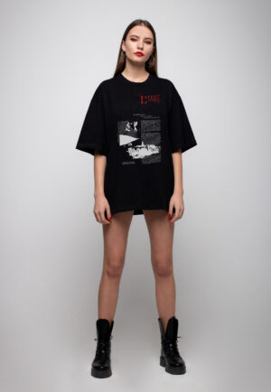 Full-body shot of a model wearing a black oversized t-shirt neat atelier with a white newspaper-style graphic and red text, paired with black combat boots