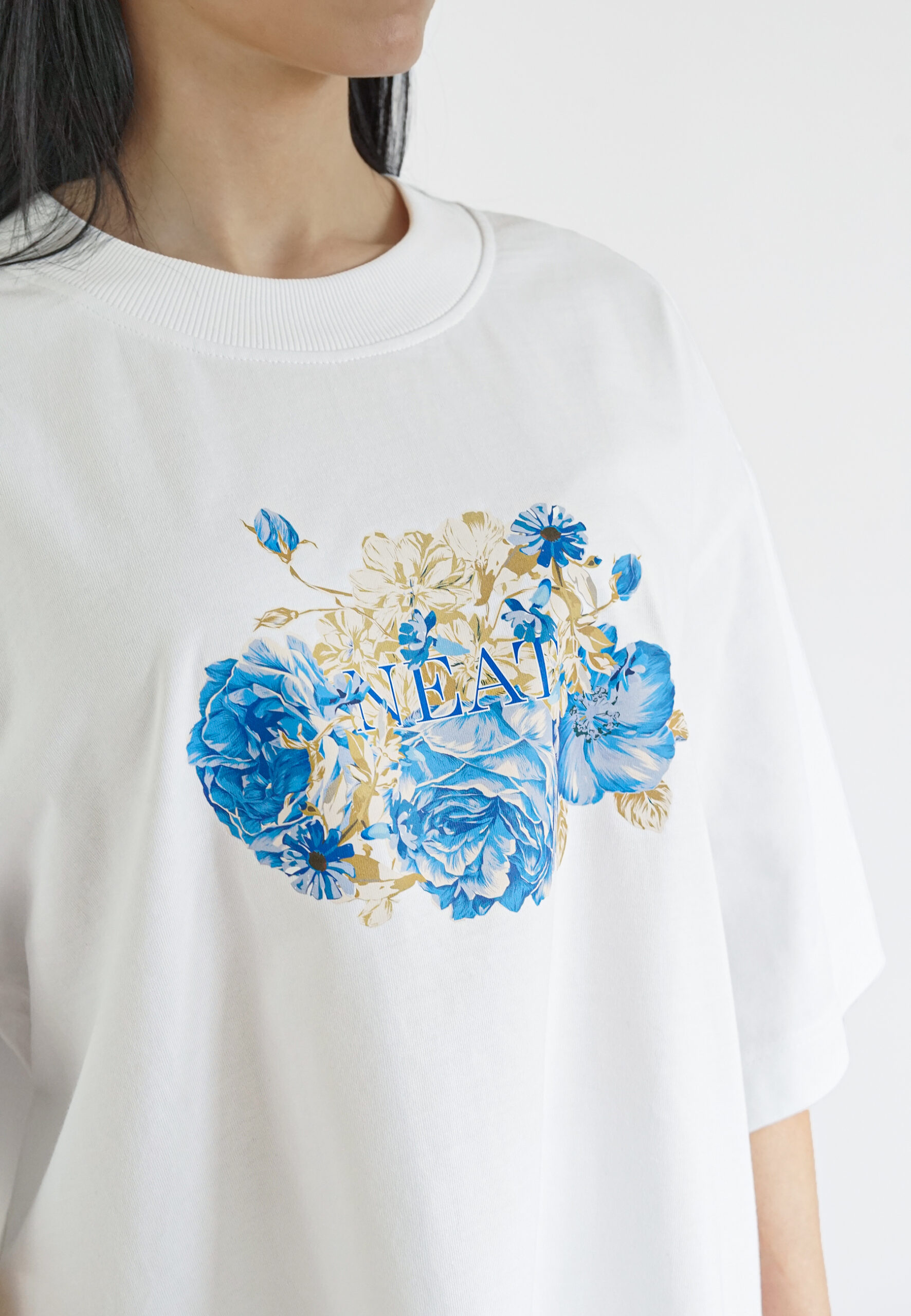 Close-up of a blue floral graphic print on a white cotton t-shirt with the brand name Neat integrated into the design.