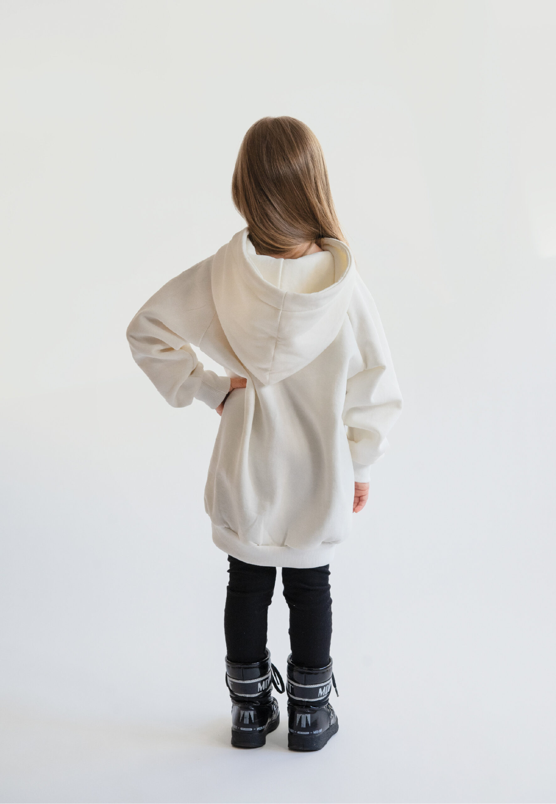 A young girl smiling and wearing a cream-colored oversized hoodie with a "Little hedgehog" illustration and Neat Atelier branding, designed for a matching mother-and-daughter look. back photo moon boots